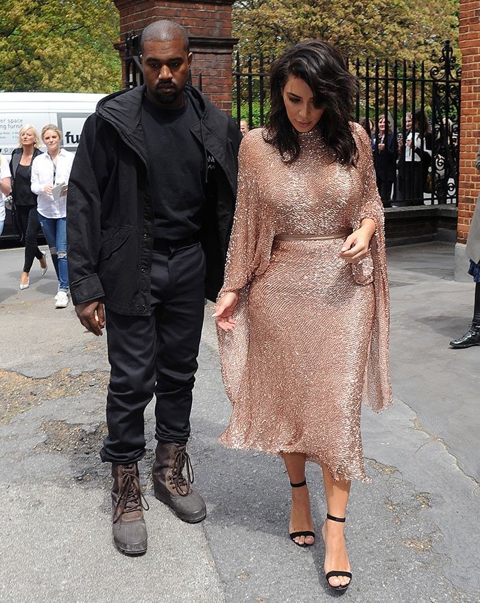 Kim Kardashian arrives in a shimmering dusty-pink Talbot Runhof dress paired with black Manolo Blahnik “Chaos” sandals, while Kanye West keeps it rugged in lace-up combat boots at the Vogue 100 Festival in London