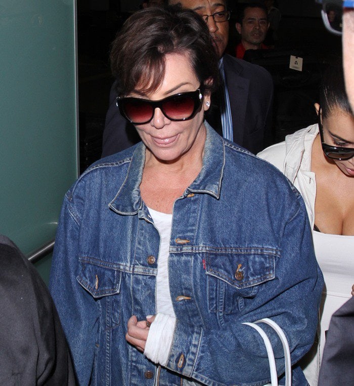 Kris Jenner keeps her airport look casual in an oversized denim jacket layered over a simple white top and finished with gradient oversized sunglasses
