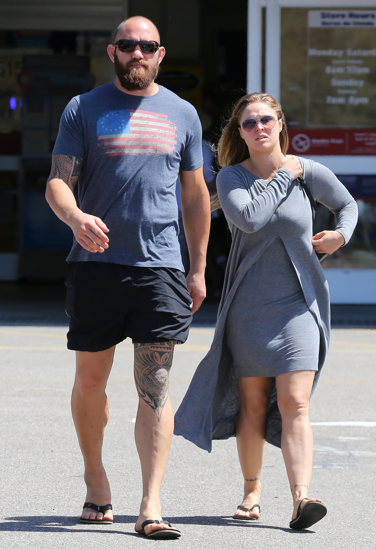 Ronda Rousey keeps it casual in a fitted gray dress and flip-flops alongside Travis Browne, whose athletic shorts and slides emphasize their striking height difference