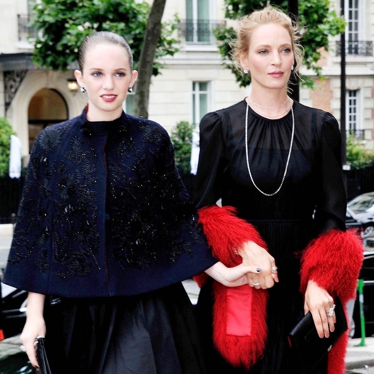 Maya Hawke looks regal in an embellished navy cape and satin skirt, while Uma Thurman stuns in a black dress with dramatic red fur cuffs at the 2014 Miu Miu Resort Collection show in Paris