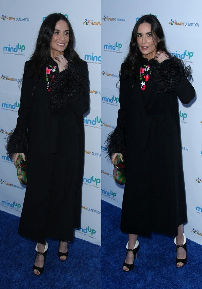 Demi Moore attends Goldie Hawn’s Love In for Kids event in a long black coat with feather-trimmed sleeves, revealing a bright floral dress and her distinctive collar-fold black heels