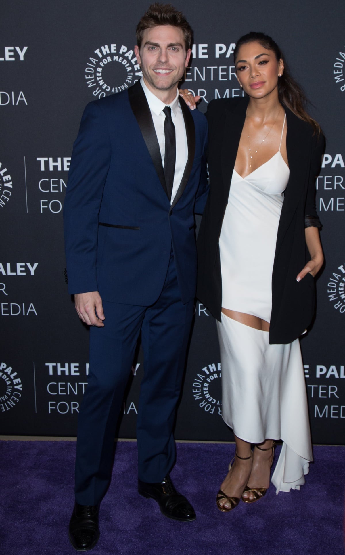Nicole Scherzinger exudes effortless elegance in a silky white slip dress paired with metallic strappy heels and an oversized black blazer, posing alongside co-star Colt Prattes at The Paley Center for Media’s “Dirty Dancing: The New ABC Musical Event” premiere and conversation on May 18, 2017, in Beverly Hills, California