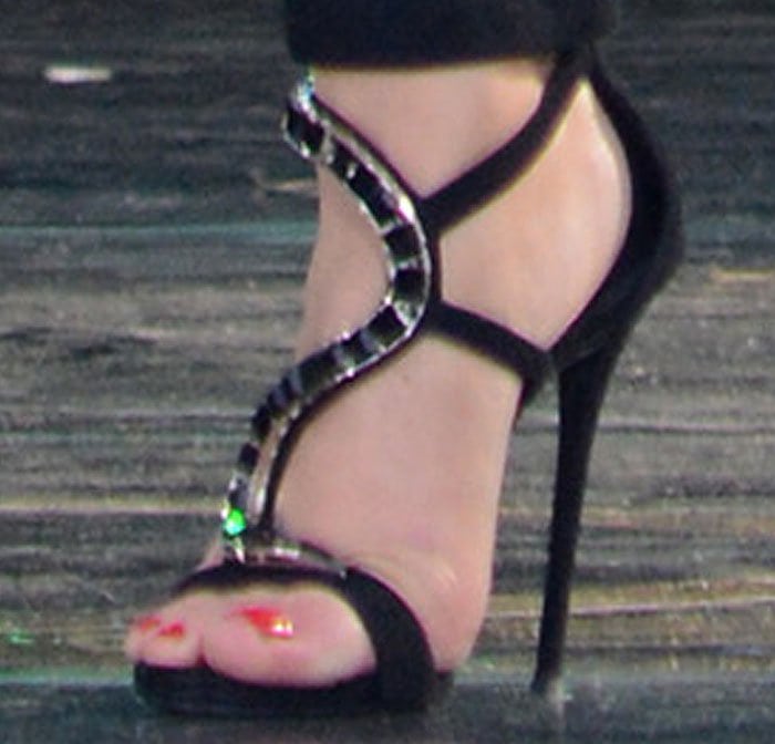 A close-up reveals the Giuseppe Zanotti “Venere” sandals, defined by their crystal-embellished serpentine straps and sky-high stiletto heel that add jewelry-like drama from the ground up
