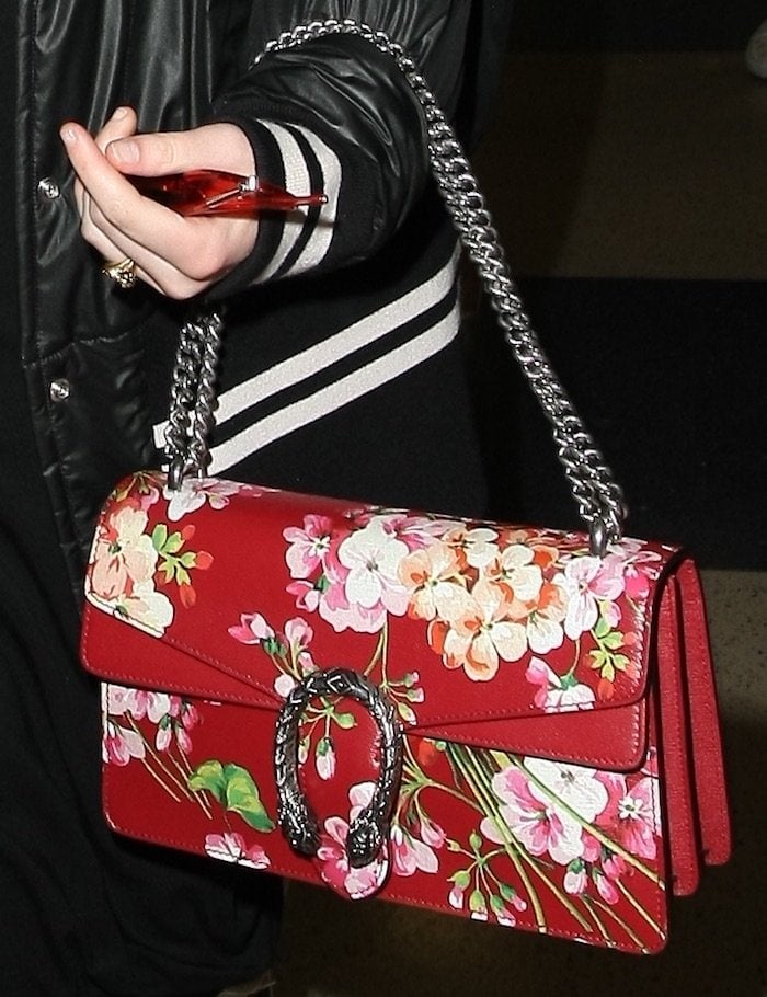 Elle Fanning adds a pop of color to her monochrome outfit with a striking red Gucci Dionysus Blooms handbag, featuring intricate floral embroidery and silver chain detailing