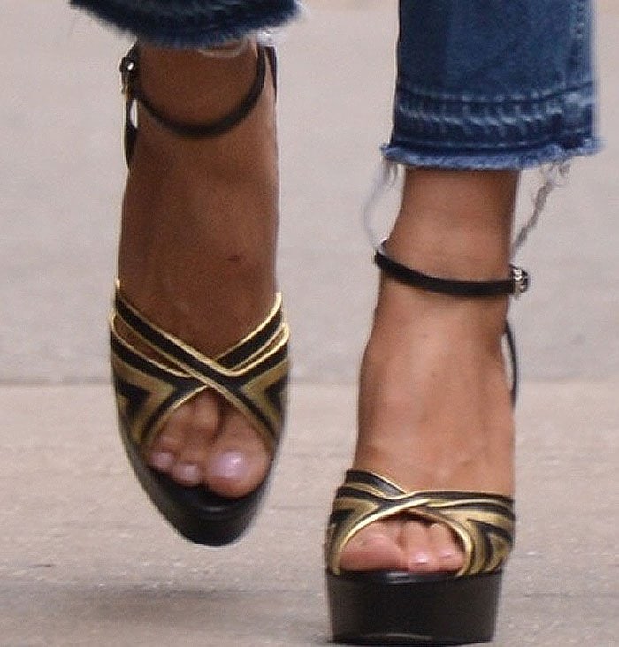Heidi Klum wears a pair of gold, metallic, open-toe Valentino sandals with a high platform and a thick ankle strap