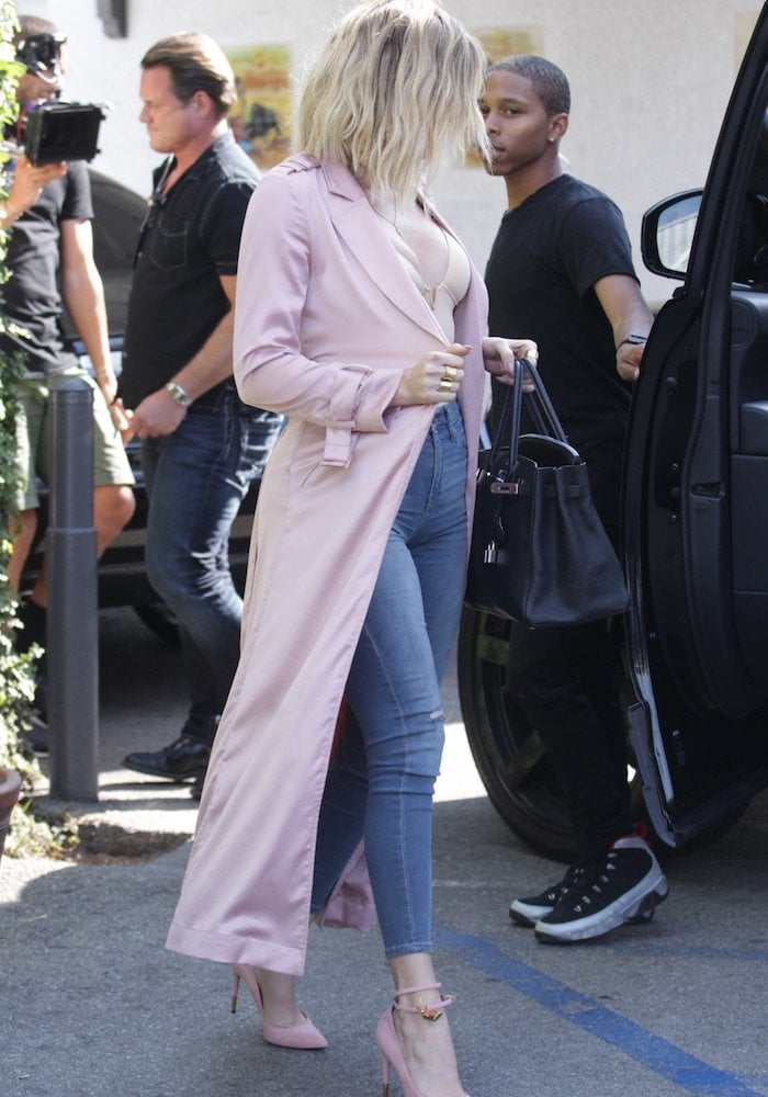 Khloé Kardashian pairs a blush satin duster with skinny jeans and pink Tom Ford padlock pumps for a sleek, feminine street-style look