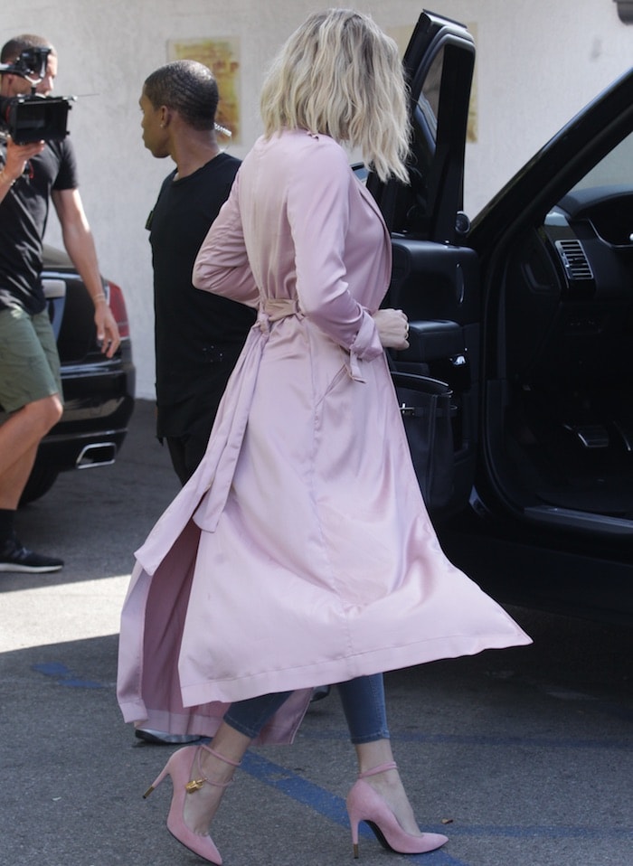 Khloé Kardashian stepped out in a House of CB “Fabienne” satin trench layered over a nude Cosabella bodysuit, Topshop Moto ripped skinny jeans, and accessories including a Graziela starburst necklace, Victoria Beckham aviator sunglasses, a Lumee illuminated iPhone case, and Tom Ford suede ankle-lock pumps