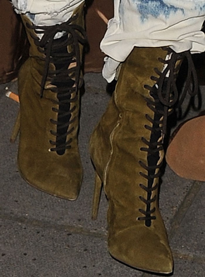 A closer look at Kim Kardashian’s olive Yeezy boots reveals their elongated pointed toes, black corset-style lacing, fitted shafts, and needle-thin stiletto heels