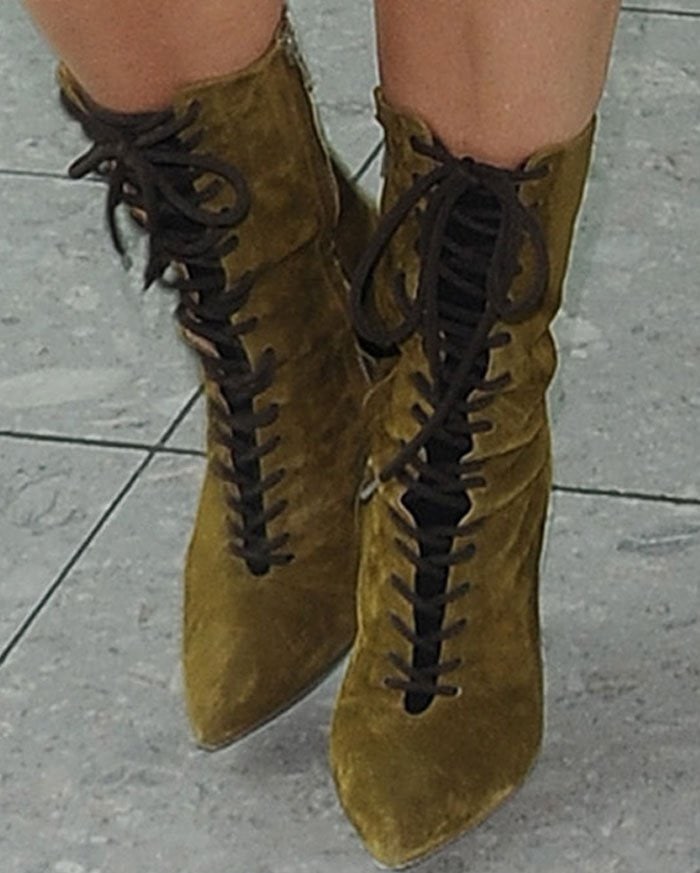 A close-up highlights Kim Kardashian’s olive suede Yeezy lace-up boots, finished with sharp pointed toes, contrasting dark laces, and slim stiletto heels