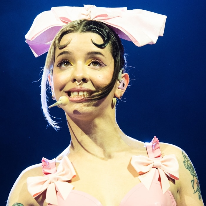 Melanie Martinez proudly embraces her prominent teeth, showcasing a captivating and endearing smile that sets her apart, while performing
