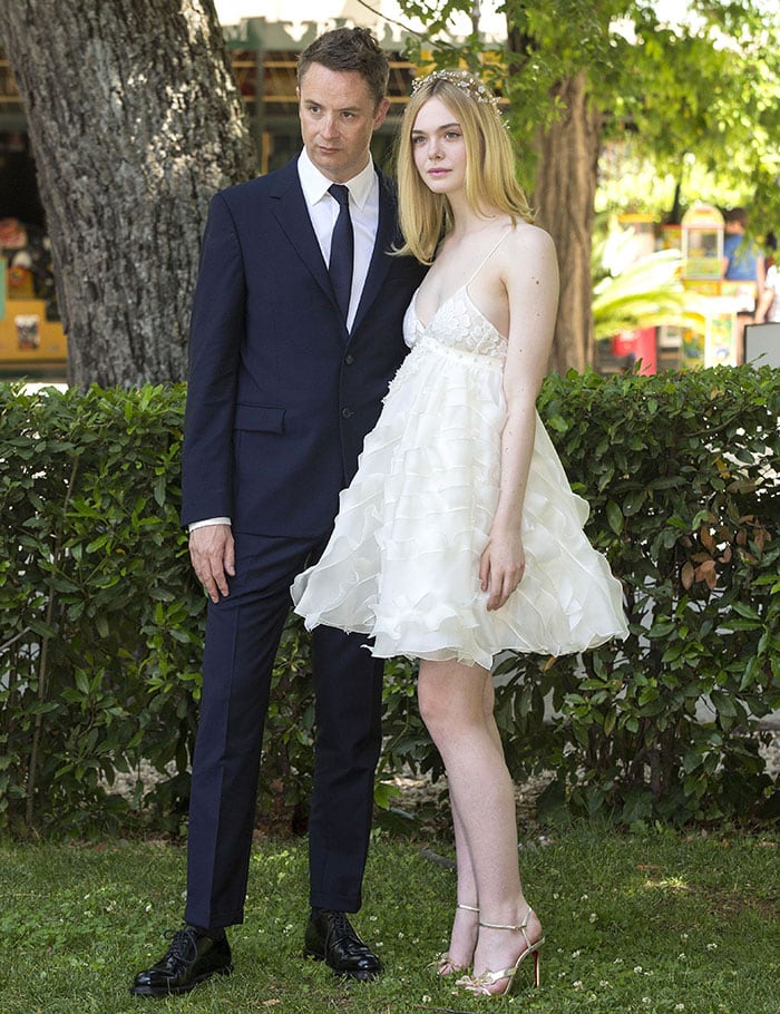 Nicolas Winding Refn keeps it sharp in a navy suit as Elle Fanning channels modern fairy-tale elegance in a ruffled ivory Giamba dress, finished with crystal-embellished gold Christian Louboutin “Bat Bat” heels at The Neon Demon Rome photocall