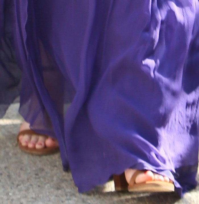 Olivia Munn’s feet peek out from beneath her flowing purple gown, revealing her brown suede Stuart Weitzman “NearlyNude” block-heel sandals