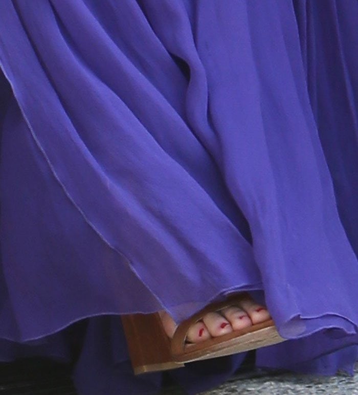 Olivia Munn’s red pedicure peeks out beneath her flowing purple gown, highlighting her brown suede Stuart Weitzman “NearlyNude” block-heel sandals with a subtle pop of color
