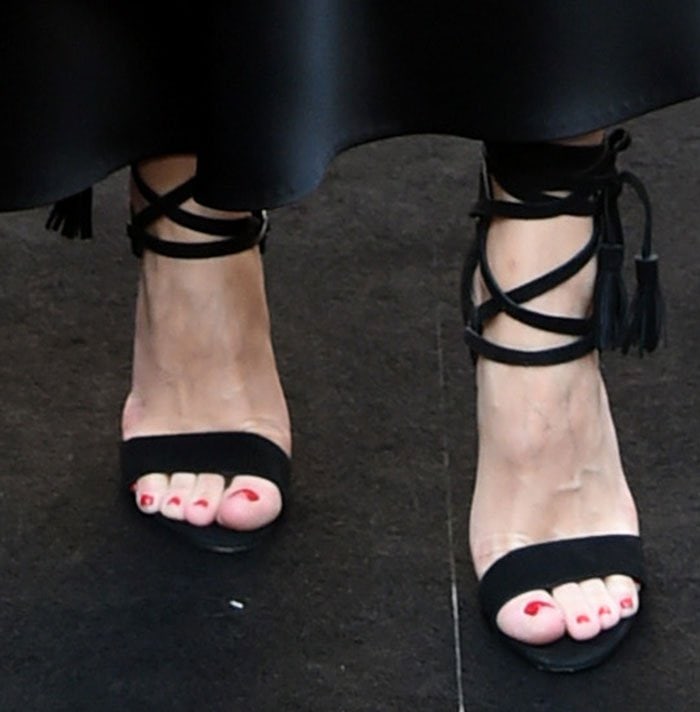 Her black Rebecca Minkoff “Riley” sandals feature slim straps and tasseled ties that wrap elegantly around her ankles
