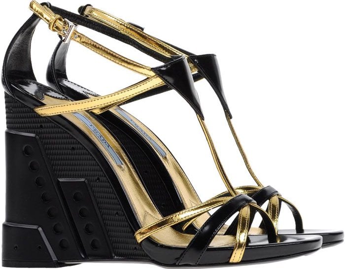 Prada’s perforated wedge sandals strike a bold contrast in glossy black leather and metallic gold straps, anchored by a sculptural wedge heel finished with industrial-inspired perforations and textured panels