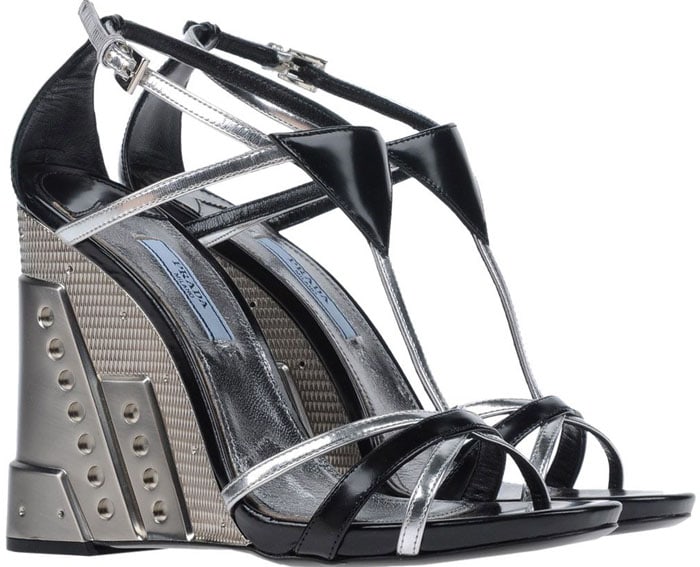 Prada’s perforated metallic wedge sandals fuse industrial edge with sculptural elegance, featuring mirrored silver straps, angular T-bar detailing, and a bold architectural wedge punctuated by signature stud-like perforations