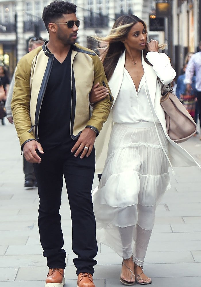 Newlyweds Russell Wilson and Ciara walk arm-in-arm through the streets of London, with Ciara's stylish post-wedding outfit—including her tiered skirt and lace-up Stuart Weitzman sandals—on full display