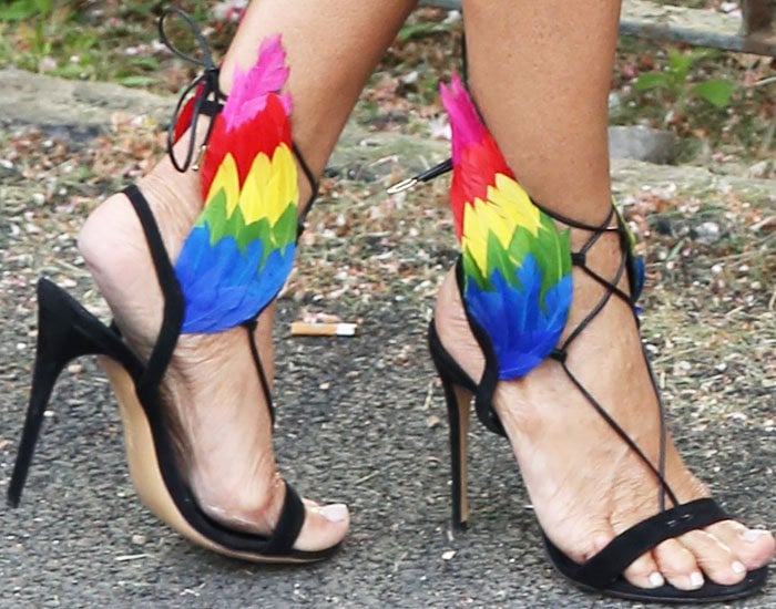 A close-up of the Ferragamo x Edgardo Osorio “Dream” sandals reveals black suede lace-up straps and striking multicolored feather wings at the ankle, adding sculptural movement and playful contrast to the sleek stiletto silhouette