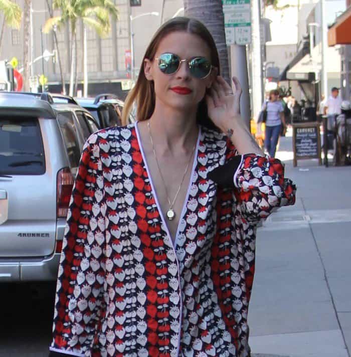 Jaime King styles her sleek, center-parted hair with mirrored aviator sunglasses and a delicate gold pendant necklace, adding polish to her bold pajama-inspired look