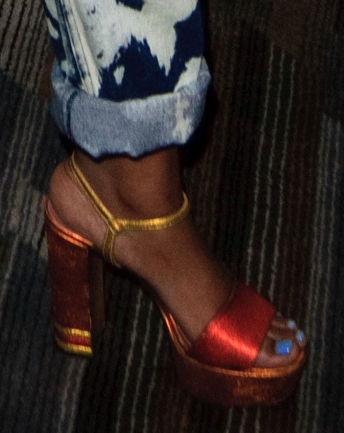 Keke’s shimmering orange and gold Bally “Clarine” sandals add vibrant contrast to her cuffed, paint-splattered jeans
