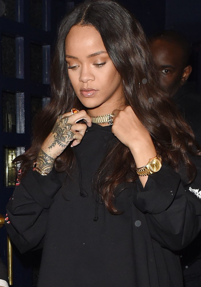 Rihanna keeps it understated up top in an oversized black Vetements hoodie dress, elevating the look with a gold choker, stacked rings, and a sleek gold watch