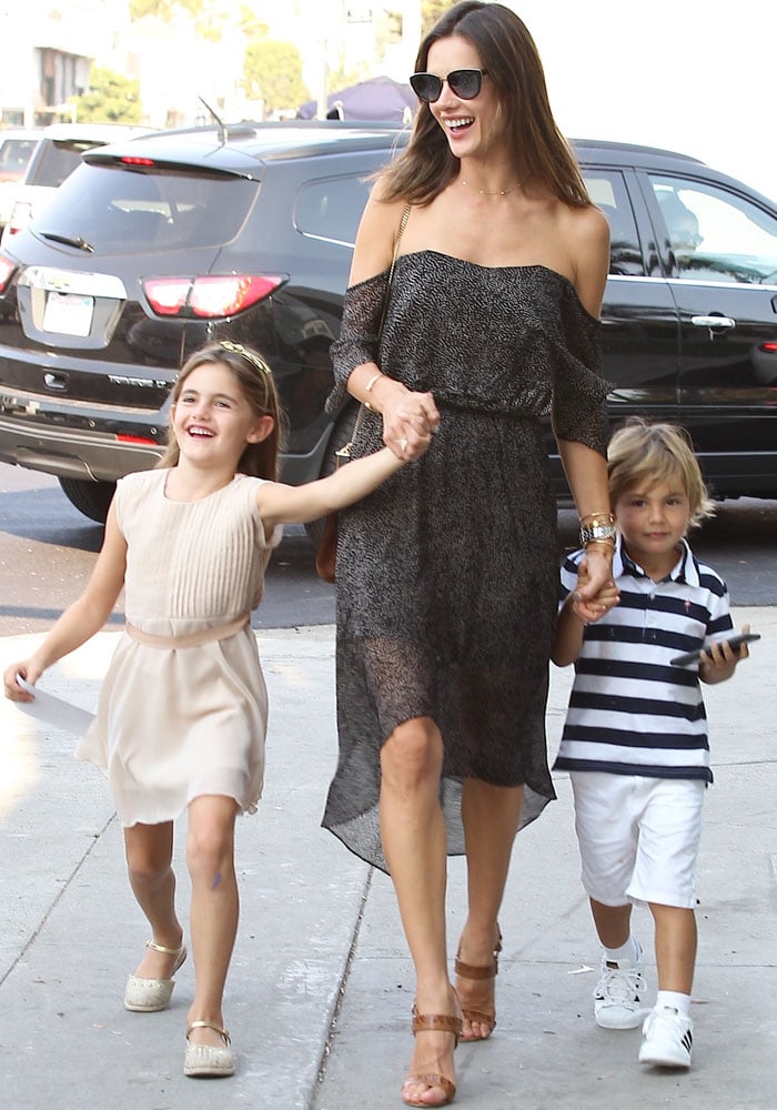Alessandra Ambrosio pairs a breezy off-the-shoulder Camilla and Marc dress with brown reptile-embossed Christian Louboutin “Sova” sandals, effortlessly balancing relaxed daytime elegance with polished, leg-lengthening minimalism as she steps out with her children in Los Angeles