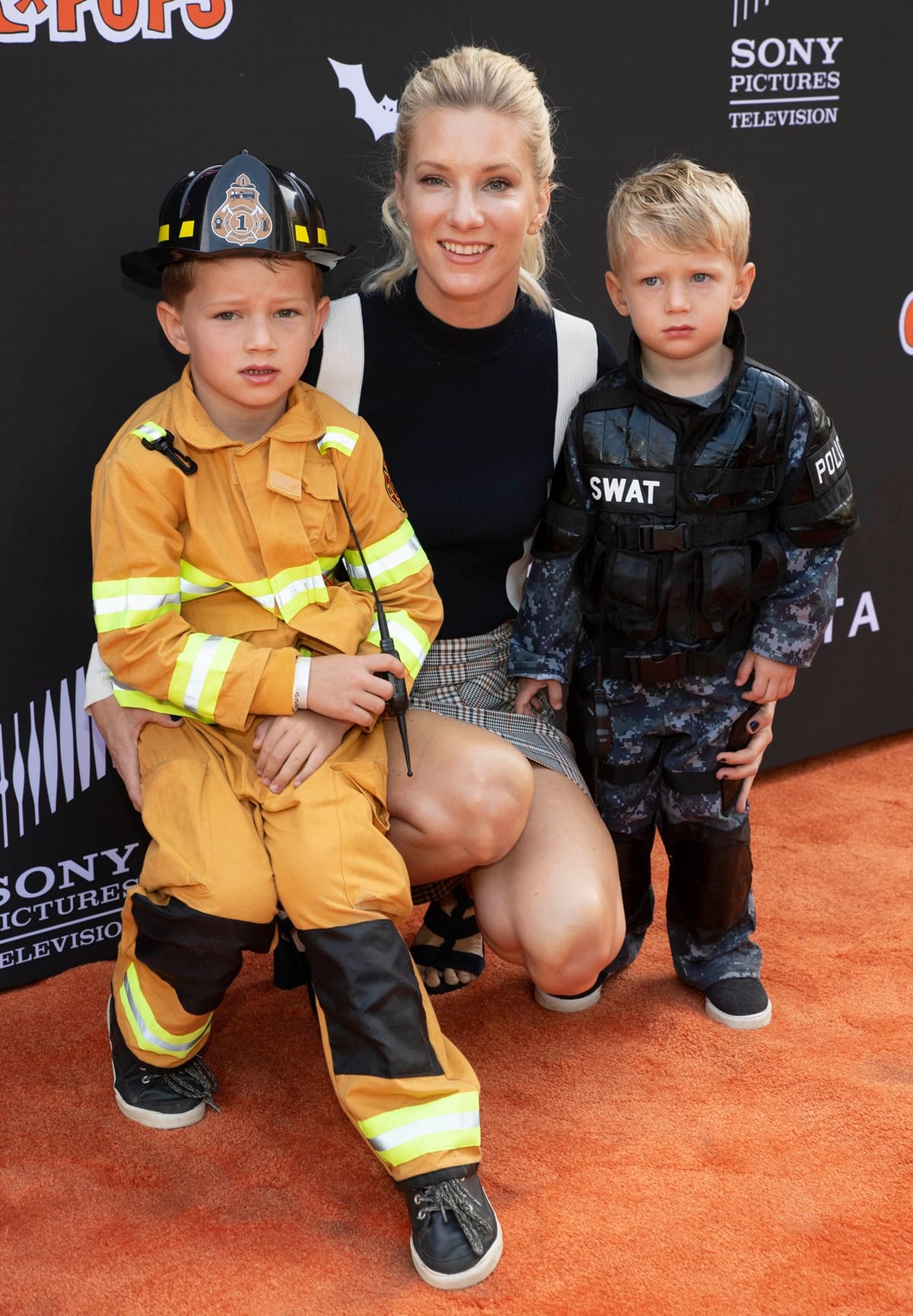 Heather Morris attends the GOOD+ Halloween Bash with sons Elijah and Owen, pairing a plaid mini skirt with strappy black sandals that show off her chic, mom-on-duty style