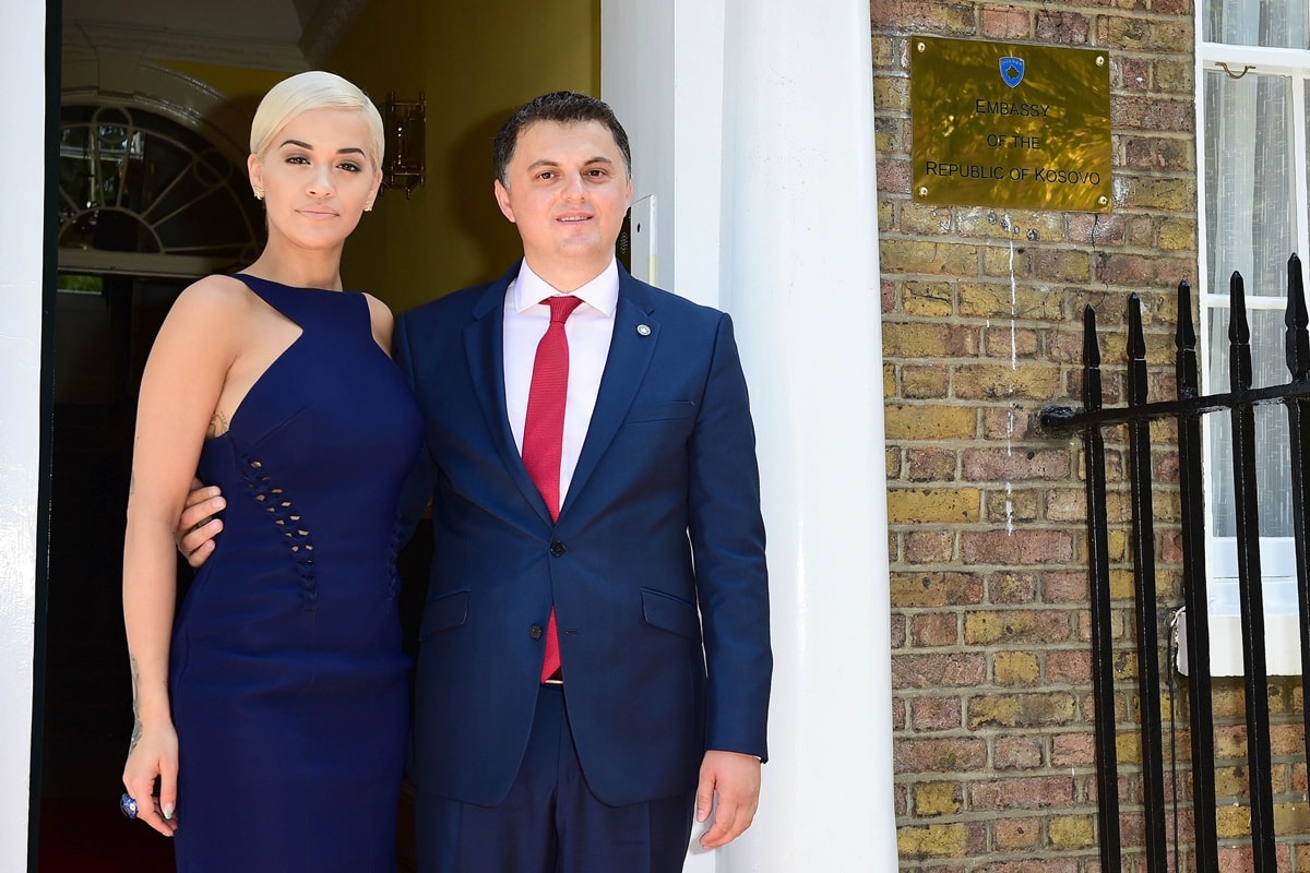 Rita Ora wears a sleek navy cutout dress as she poses with Lirim Greiçevci, Ambassador of the Republic of Kosovo, during her 2015 honorary ambassadorship ceremony in London