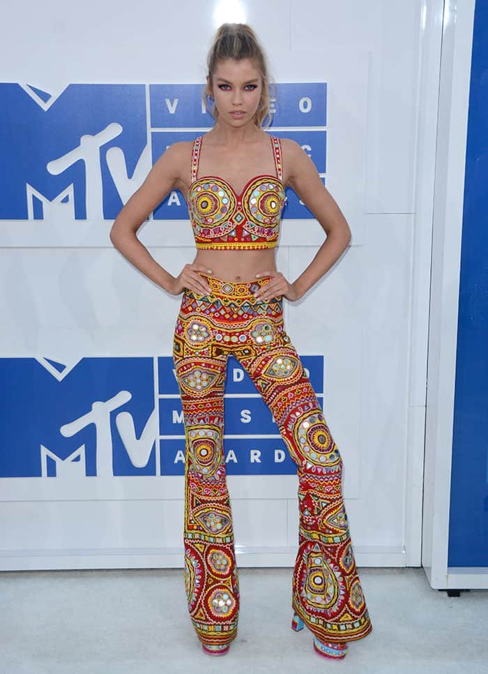 Stella Maxwell poses at the MTV Video Music Awards in a vibrant Moschino Resort 2017 set, anchored by towering platform heels that extend the look’s bold, retro proportions