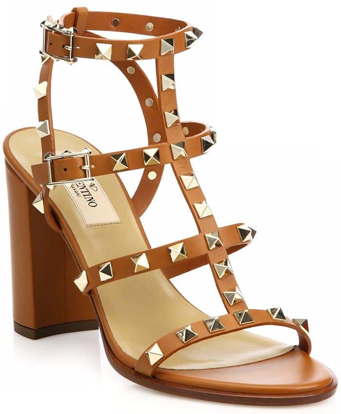 Valentino’s “Rockstud” block-heel T-strap sandals in cognac leather showcase the house’s iconic pyramid studs across a caged silhouette, while the sturdy stacked heel and double-buckle ankle straps add structure and all-day wearability (originally retailing for $1,045)