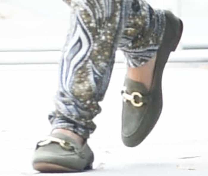 A close-up highlights her olive suede loafers with gold horsebit hardware, grounding the flowing patterned joggers with a tailored, equestrian-inspired flat