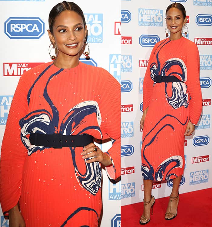 Alesha Dixon makes a bold fashion statement in a vivid orange pleated midi dress with abstract navy prints, cinched at the waist with a black belt, and elevates the look with metallic chain-detailed Gucci "Ophelie" sandals