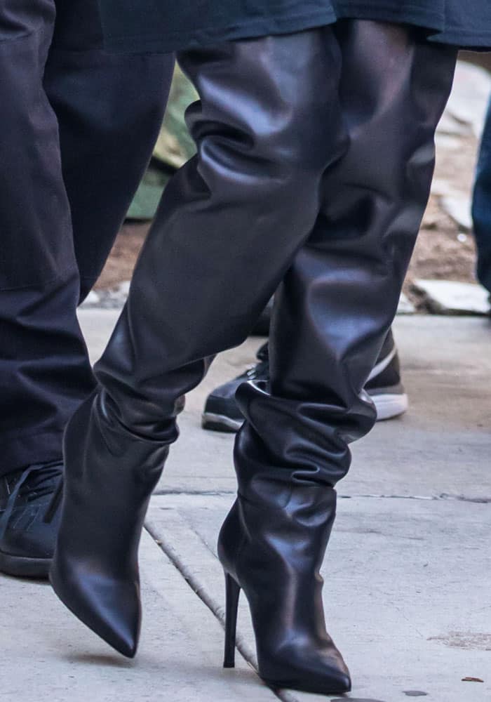 Kim Kardashian completes her monochrome look with slouchy black over-the-knee leather boots, featuring sharply pointed toes and slender stiletto heels that create a sleek, elongated silhouette