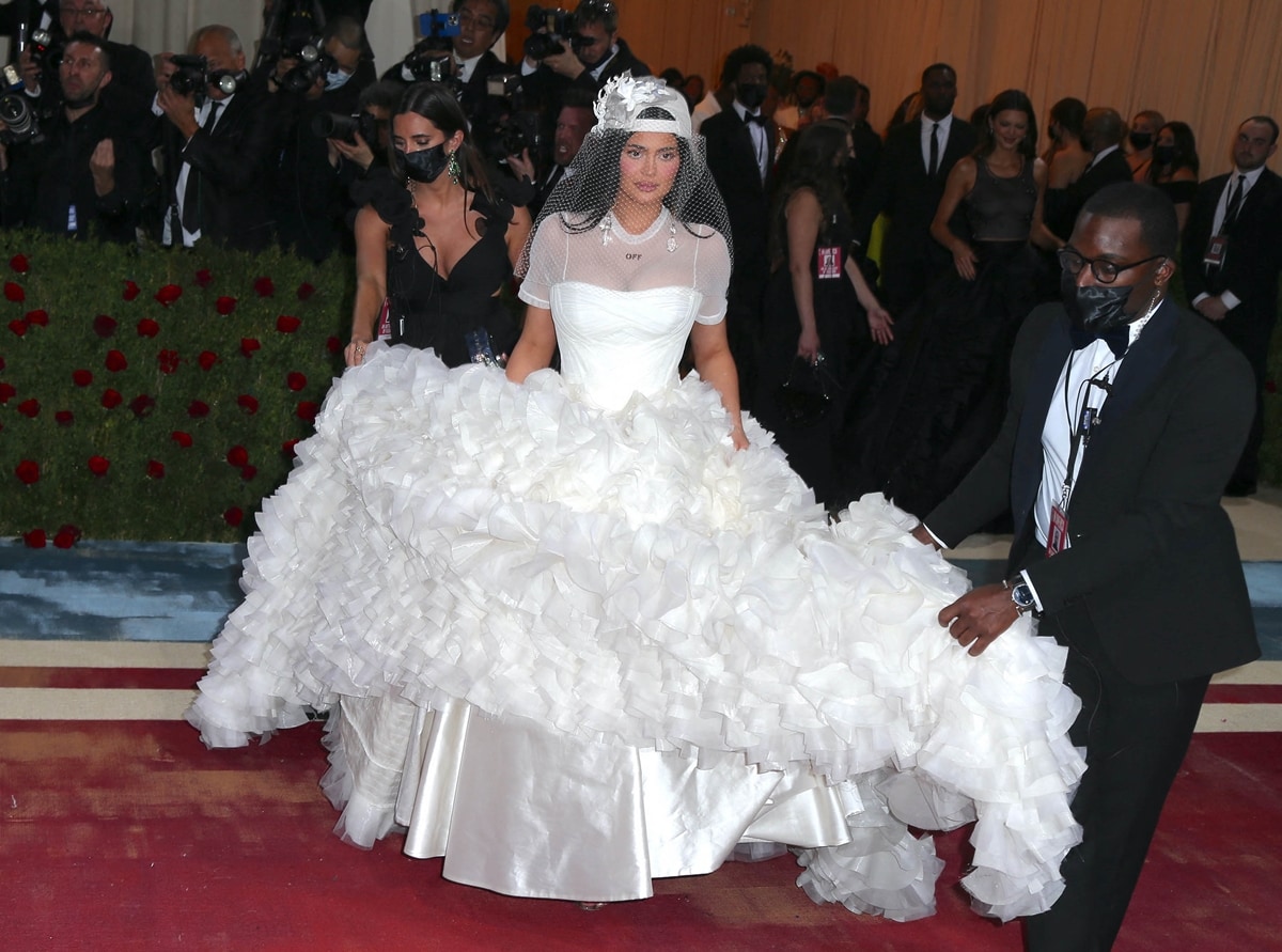 Kylie Jenner honored the late Virgil Abloh at the 2022 Met Gala with a dramatic Off-White bridal gown featuring a voluminous ruffled skirt, mesh T-shirt overlay, and a backward baseball cap with a veil
