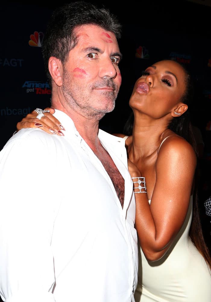 Mel B plants a kiss on Simon Cowell backstage, leaving lipstick marks across his face and punctuating the night’s now-infamous on-air water-splash moment with her signature fearless humor