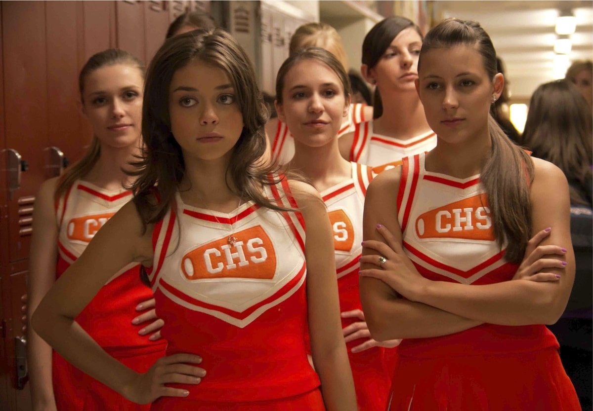 Sarah Hyland, standing front and center as head cheerleader Claire Mathews in Struck by Lightning, wears a bright red and white CHS cheer uniform that highlights her petite 5′1″ (154.9 cm) frame and youthful screen presence