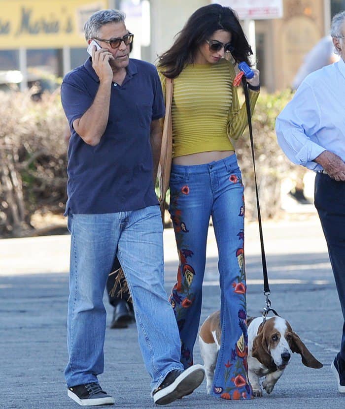 Amal Clooney embraces ‘70s chic in embroidered Alice + Olivia bell-bottom jeans and a mustard crop top, while George Clooney keeps it classic in casual denim and sneakers during their laid-back outing