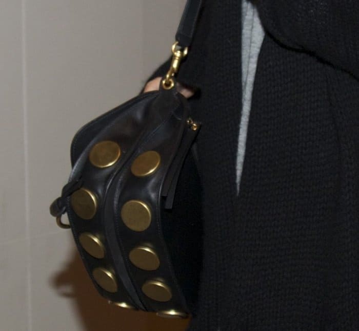 Chrissy Teigen carries the Chloé “Kurtis” bag, a chic satchel accented with bold oversized gold studs and supple black leather for a modern, edgy finish
