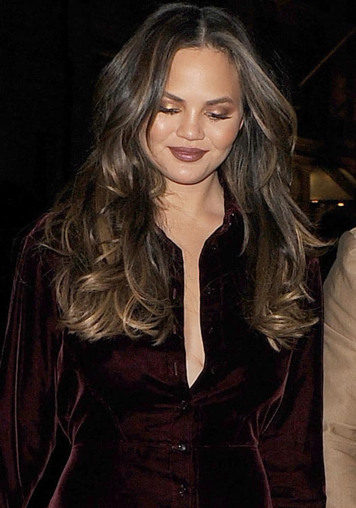 Chrissy Teigen looked stunning in a striking burgundy velvet shirt dress in London