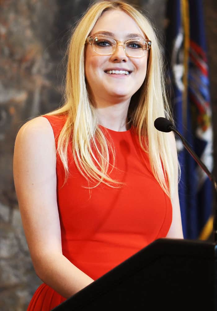 Dakota Fanning smiles at the podium in a sleeveless red dress as she addresses attendees during the Empire State Building lighting ceremony in New York City