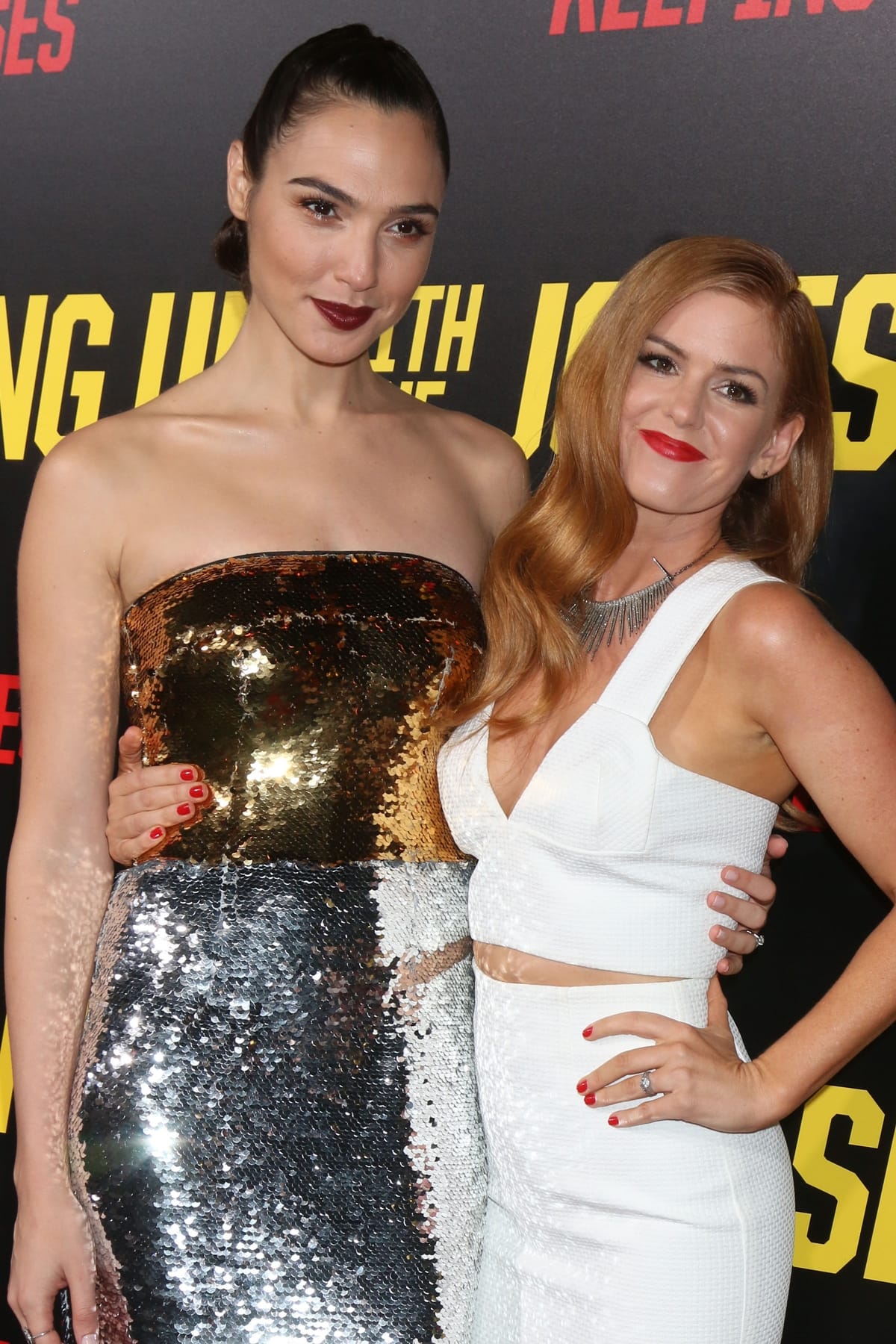 At the Keeping Up with the Joneses premiere, Gal Gadot stunned in a strapless gold-and-silver sequined Dolce Gabbana dress, towering over Isla Fisher in a chic white crop top and skirt ensemble