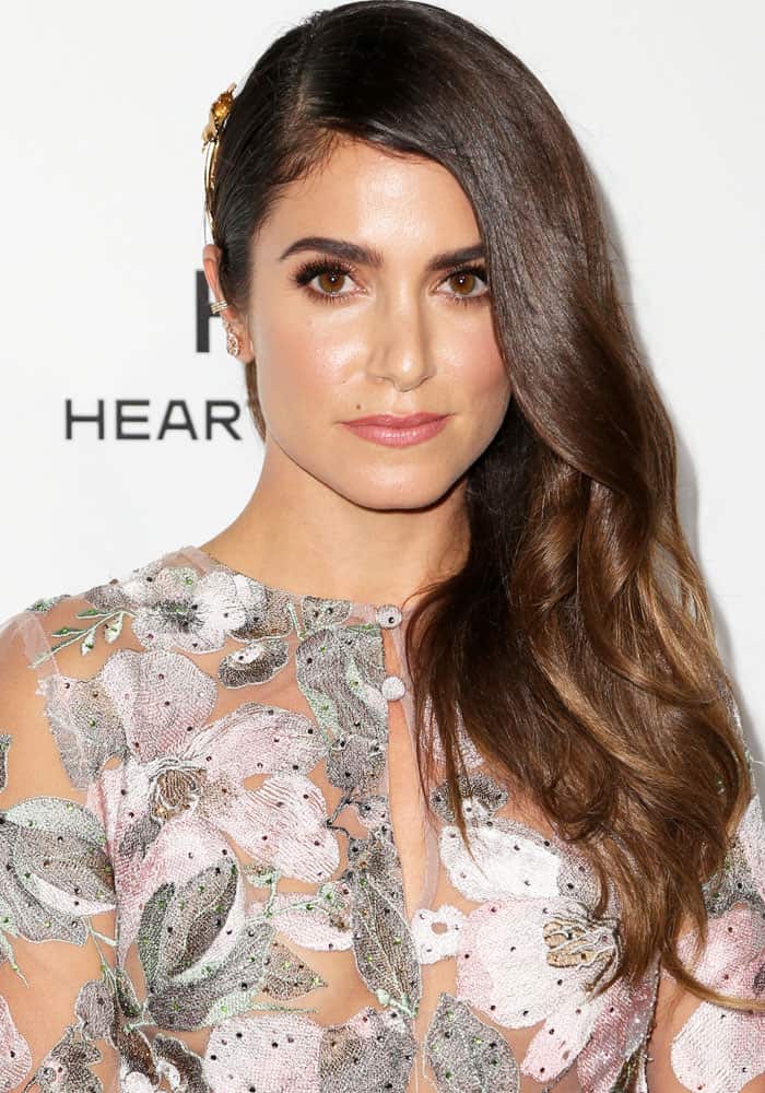 Nikki Reed’s beauty look stays soft and luminous, with side-swept waves and understated makeup complementing the delicacy of her sheer embroidered gown