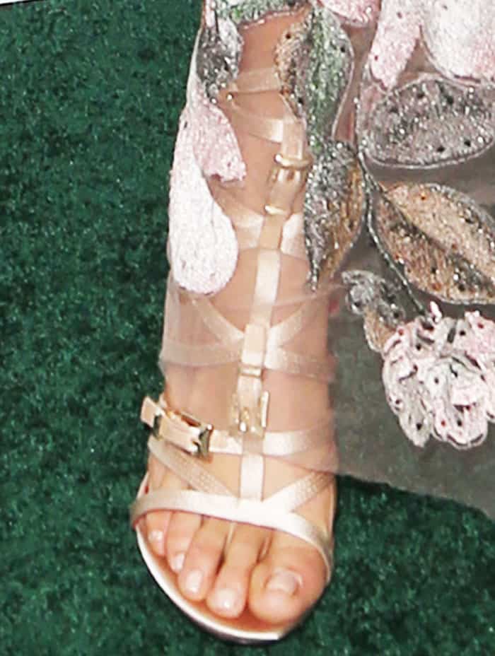 A close-up reveals the barely-there Cesare Paciotti sandals, where slim nude straps and metallic hardware add subtle edge without distracting from the gown