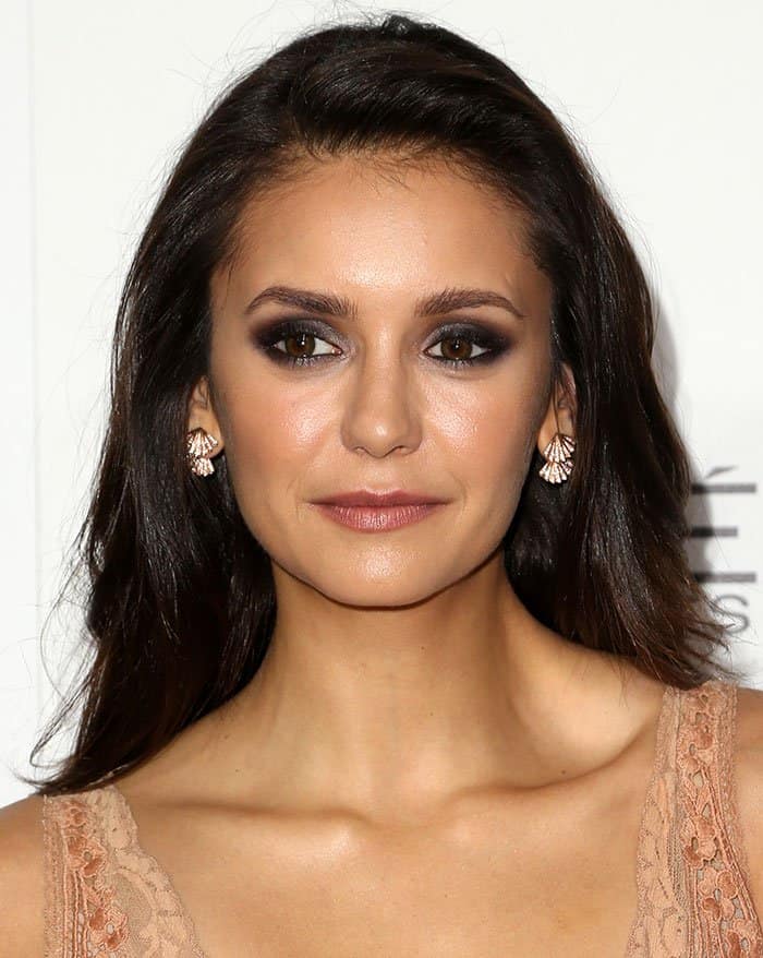Nina Dobrev complements her look with smoky eye makeup, softly defined brows, and a natural nude lip