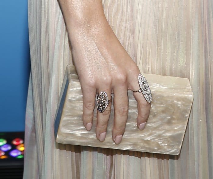 Katy Perry accessorizes her look with statement rings featuring intricate detailing and a chic marble clutch