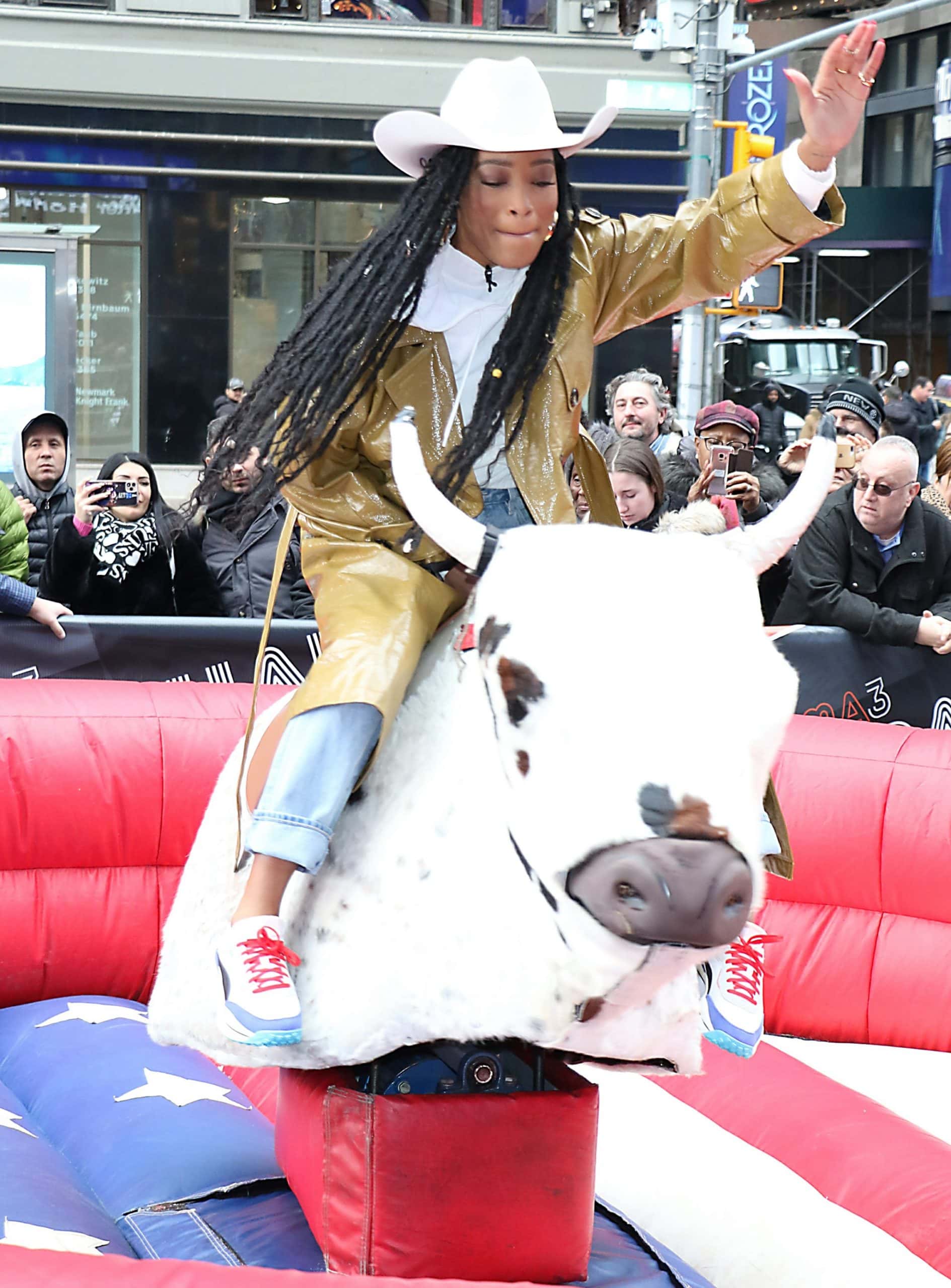 Keke Palmer embraces western-chic fun in Times Square, pairing bright red-and-blue sneakers with a cowboy hat and glossy trench as she rides a mechanical bull on Good Morning America