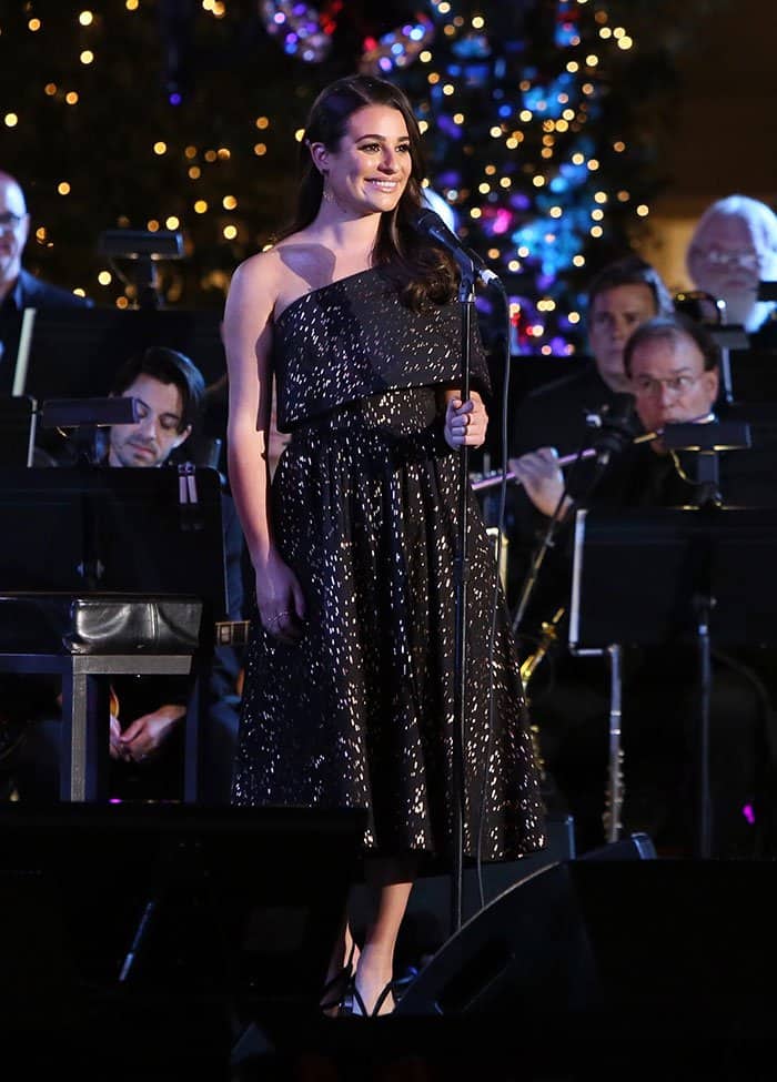 Lea Michele brings festive elegance to the stage in a shimmering one-shoulder Lela Rose dress paired with Sophia Webster's black suede “Madame Butterfly” sandals