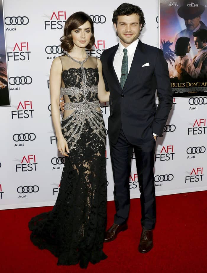 Lily Collins stuns in a sheer black lace Reem Acra gown while Alden Ehrenreich keeps it classic in a sharp navy suit at AFI FEST 2016’s Rules Don’t Apply premiere in Hollywood