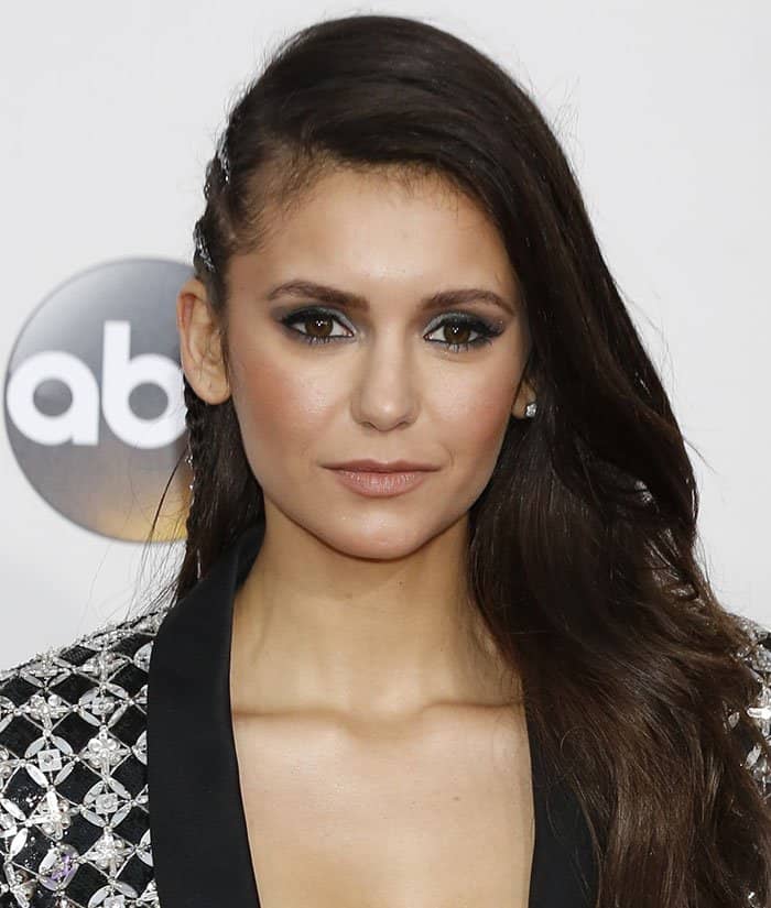 Nina Dobrev enhances her smoky eye makeup with a nude lip and subtle stud earrings, letting her dark brown eyes take center stage