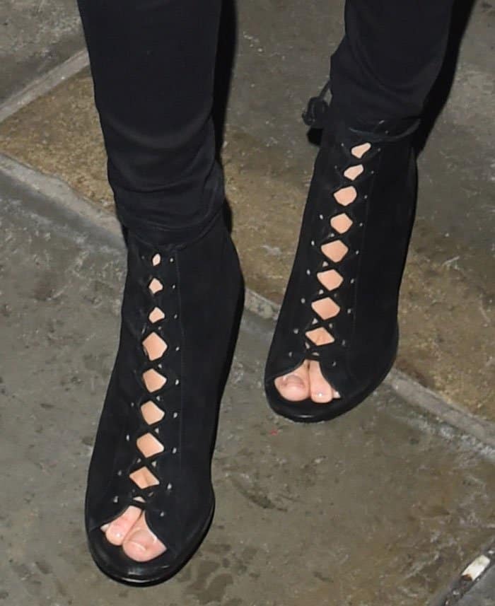 Poppy Delevingne completes her look with Coach 'Lena' booties, featuring black suede, crisscross lace-up details, flower charms, peep toes, and 4.5-inch heels